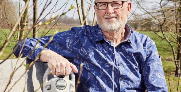 Jan Cornelissen zit op een tuinbank met een zuurstoftank naast zich