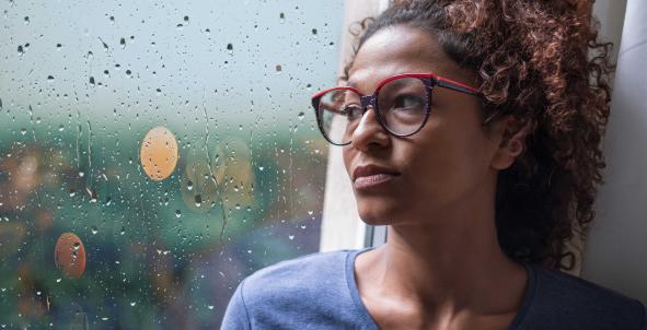 Een vrouw zit bij het raam en kijkt bezorgd en verdrietig naar buiten