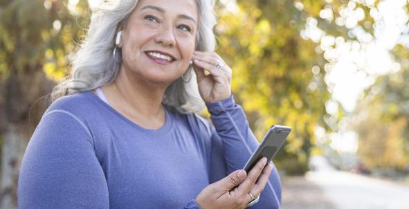 Mevrouw gaat lopen en podcast luisteren, paars shirt, telefoon in haar hand