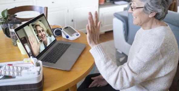 Een vrouw zwaait naar haar arts op haar laptopscherm, digitale zorg