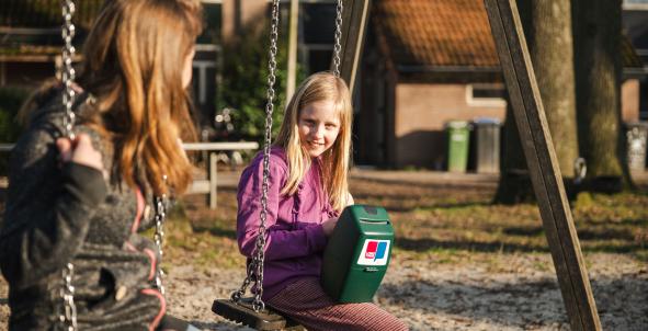 Kind zit op schommel met collectebus in haar hand