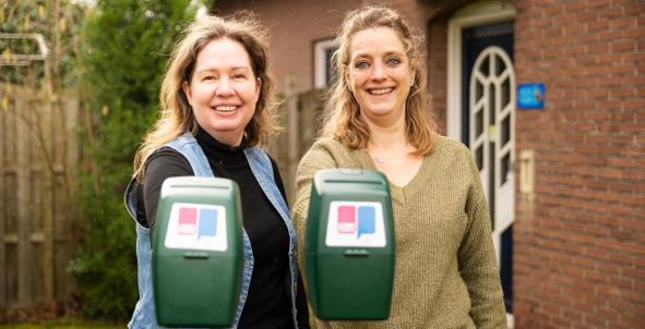 Twee vrouwen laten lachend de collectebus van Longfonds zien