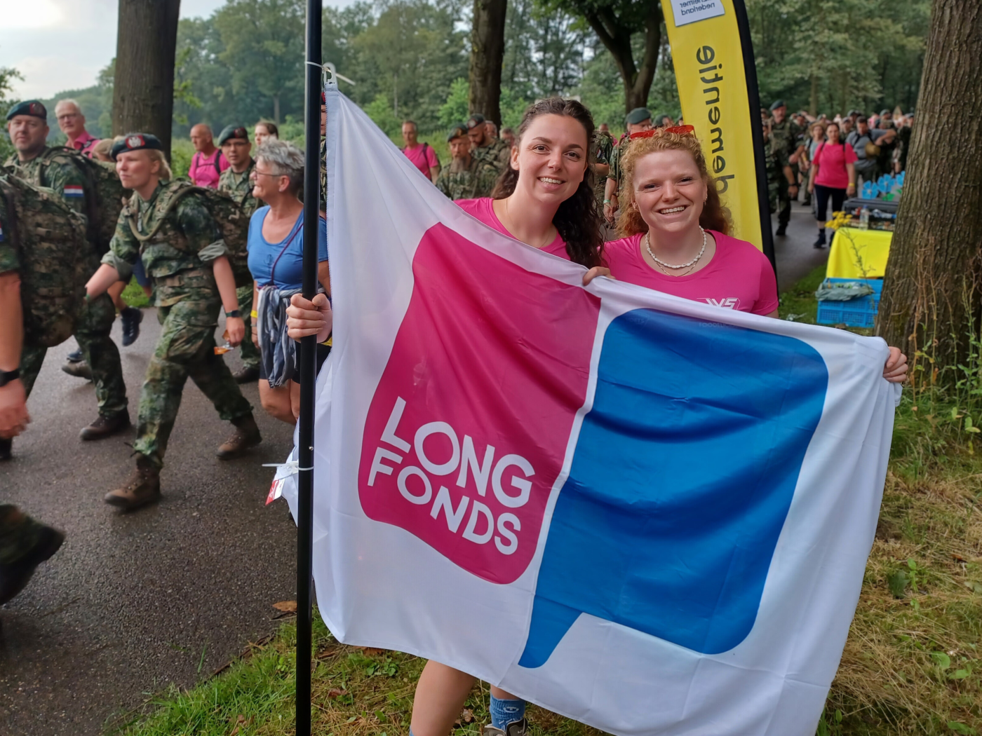 Twee zussen houden de Longfonds-vlag omhoog tijdens Nijmeegse Vierdaagse
