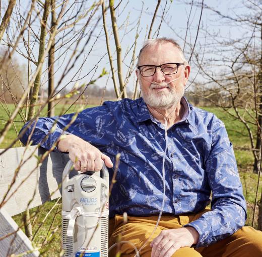 Jan Cornelissen zit op een tuinbank met een zuurstoftank naast zich