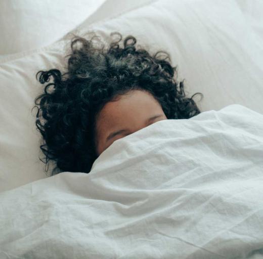 Een vrouw ligt onder de dekens in bed, alleen haar haar en voorhoofd is zichtbaar