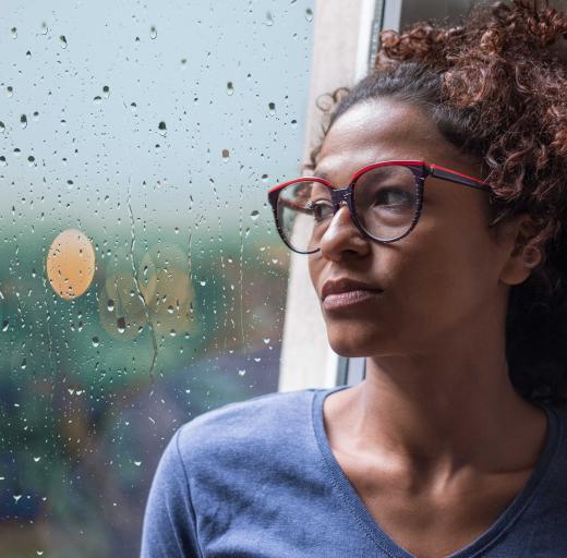 Een vrouw zit bij het raam en kijkt bezorgd en verdrietig naar buiten