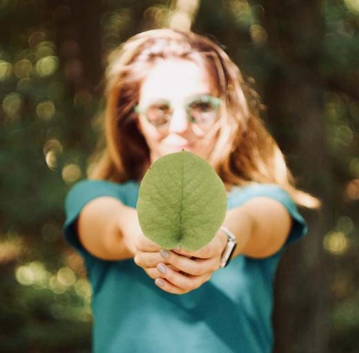 Vrouw houdt een groen blaadje voor zich uit, staat in de zon. Groen doen, 7 tips voor duurzaamheid met een longziekte.