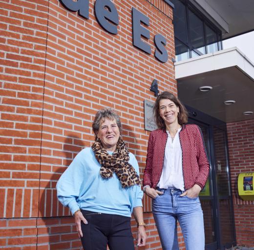 Ellie staat naast haar praktijkondersteuner Merel voor een stenen muur