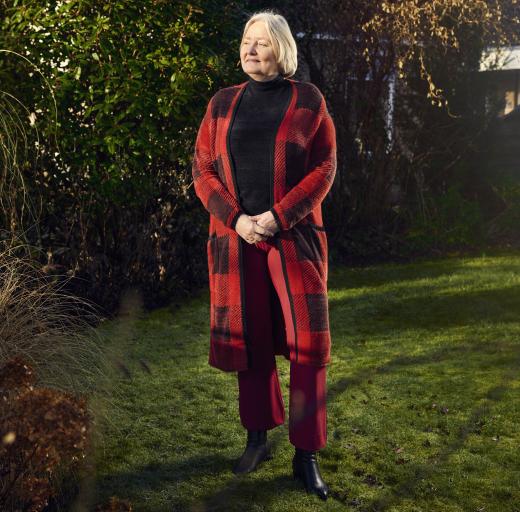 Ellen Rusch draagt een rood vest en staat in haar tuin
