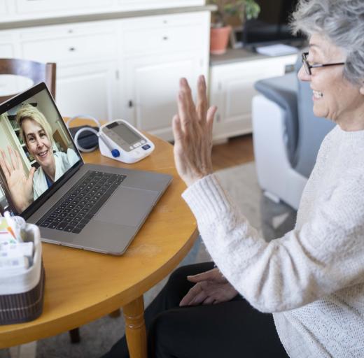 Een vrouw zwaait naar haar arts op haar laptopscherm, digitale zorg