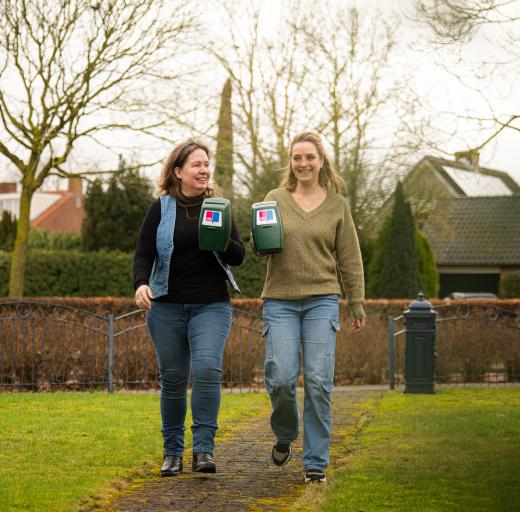 Twee vrouwen laten lachend de collectebus van Longfonds zien