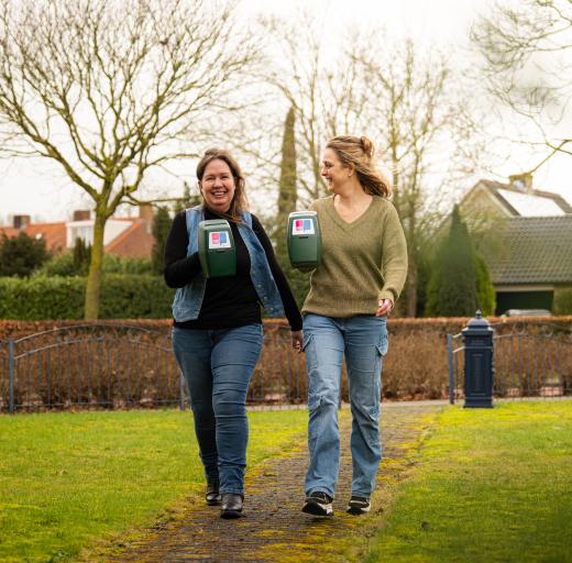 Twee vrouwen laten lachend de collectebus van Longfonds zien