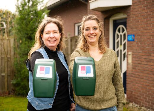 Twee vrouwen laten lachend de collectebus van Longfonds zien