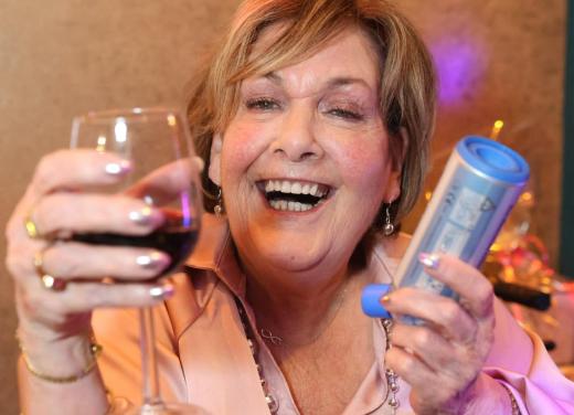 Lachende vrouw met zuurstofslangetje heeft een glas wijn en inhalator vast